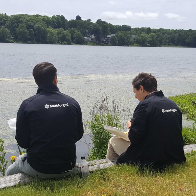 Picture of two team members in front of a lake with their Markforged jackets on